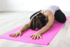 Image of a woman on a pink yoga mat stretching with crossed legs