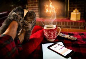 Image of feed in slippers with coffee, phone and remote control beside the and a fire in the background